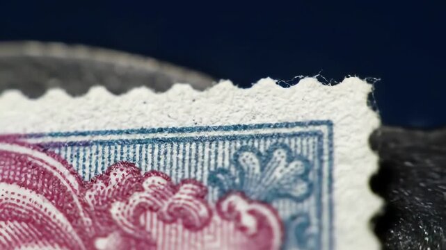 Close-up of a vintage postage stamp with a blue and pink ornate pattern and perforated edges, on a dark blue background