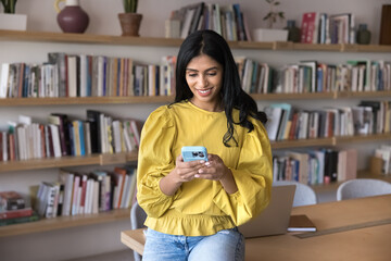 Young Indian woman, office employee or university student using smartphone in modern office,...