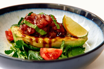 A fresh and vibrant dish featuring grilled avocado topped with a flavorful salsa, fresh basil, and lime, perfectly presented on a bed of greens and tomatoes.