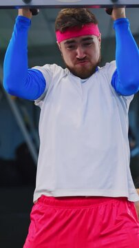 Caucasian fitness woman training weak bearded man training in the gym exercising pull ups going hard intense workout. Funny couple. Workout.