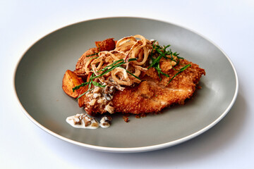 Crispy Fried Fish Fillet Garnished with Fried Onions and Accompanied by Golden Roasted Potatoes on a Stylish Plate