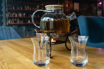Golden hour tea ritual featuring herbal tea in a glass teapot symbolizing harmony warmth and shared moments of joy. Glass teapot with herbal tea and two glasses on a wooden table.