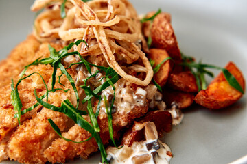 Crispy Chicken Cutlet Served with Savory Mushroom Sauce and Crispy Onion Strips on a Plate of Deliciously Roasted Potatoes and Fresh Green Herbs