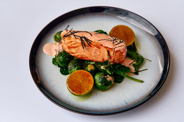 Delicate Salmon Fillet Served on a Bed of Fresh Spinach, Accompanied by Brussels Sprouts and Garnished with Citrus Slices for an Exquisite Culinary Experience