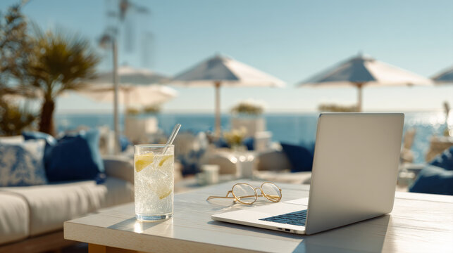 A refreshing glass of lemonade, stylish glasses, and an open laptop sit on a table at a luxurious outdoor resort lounge overlooking the ocean, embodying remote work, vacation, and a balanced lifestyle