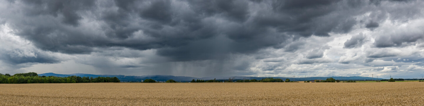 Panoramansicht eines &uuml;ber das Land ziehenden Unwetters mit Starkregen und grauer-schwarzer Wolkendecke mit bestelltem Acker im Vordergrund