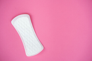 A single white sanitary pad is isolated on a plain pink background, showing its texture and shape...