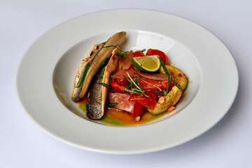 A Delicious Gourmet Dish Featuring Grilled Fish, Fresh Vegetables, and Zesty Lime on a White Plate Decorated with Garnishes and Herbs
