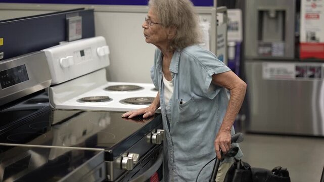 A senior woman uses her walker to browse kitchen appliances in a hardware store. She seems focused on finding the right items for her home remodeling project.