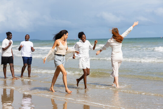 Group of people enjoying summer outdoor activities on beach with joyful expressions walking and playing near water under partly cloudy sky creating lively atmosphere