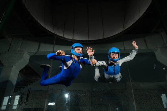A male instructor teaches a woman how to fly in a wind tunnel. Free fall simulator.