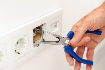 Man fixing power sockets with pliers indoors, closeup