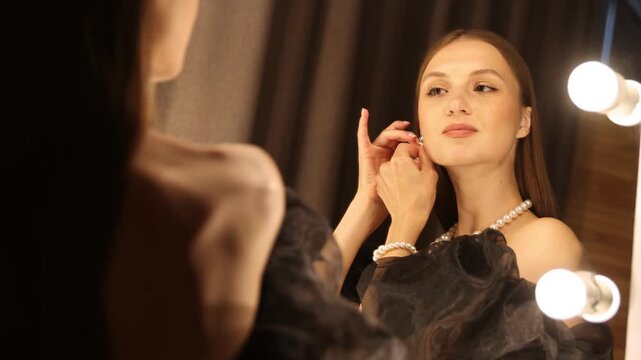 Woman wearing beautiful earrings while getting ready near mirror indoors, camera moving up