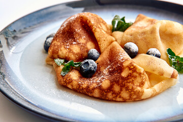 Deliciously Folded Crepes Generously Topped with Fresh Blueberries and Mint Leaves, Perfectly Served on a Elegant Blue Plate for a Delightful Dessert Experience