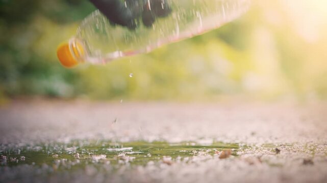 Hand in black latex glove picking up plastic bottle from puddle on asphalt slow motion environmental cleanup