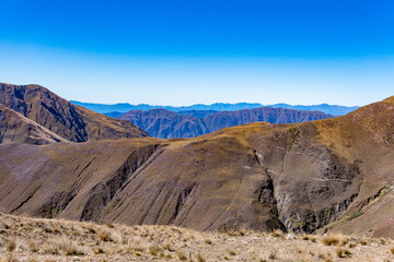 Panoramic landscape of dry, rolling Andean peaks stretching to the horizon under a clear blue sky.
