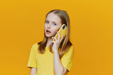 Young girl with blue eyes talking on a yellow phone, wearing a bright yellow t shirt against a...