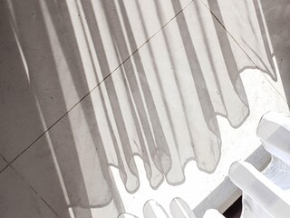 Abstract play of sunlight and shadow from curtains on a textured light floor, creating striped...