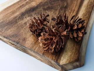 Three natural pine cones resting on a rustic wooden cutting board, with a clean white background....