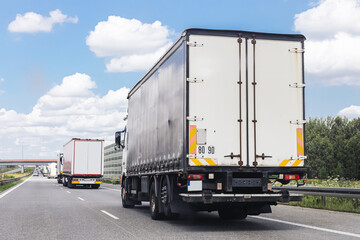 Cargo trucks on highway road. Transportation and logistics scene. Freight transport in motion. Delivery service by lorries. Industrial shipping concept. Vehicles driving under blue cloudy sky.