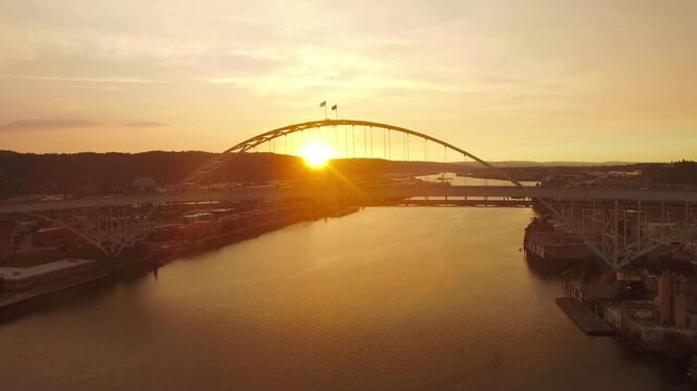 The sun sets behind a bridge over a river in portland, oregon