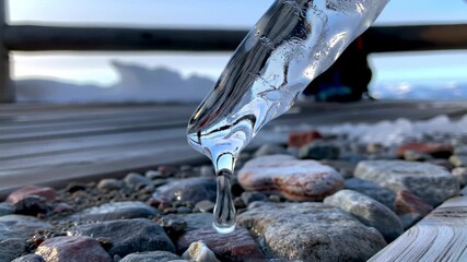 Close-up shot of a melting icicle, dripping water against a backdrop of natural stones and a - Powered by Adobe
