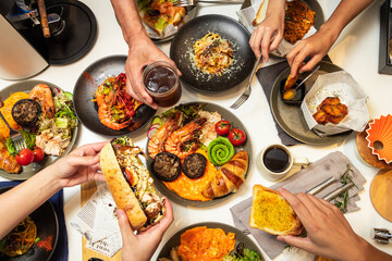 Captured from a bird's-eye view, five or six people are dining together at a Western-style restaurant, enjoying spaghetti, croissants, chicken wings, coffee, and other dishes.