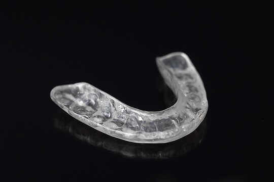 Clear night dental guard lying on black background. Used to prevent teeth grinding and protect enamel during sleep. Minimalist composition, oral health and hygiene concept.
