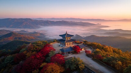 Traditional Korean mountain house and old temple pagoda surrounded by red and orange maple trees in autumn forest, with sunrise mist, distant sea, and golden hour light over peaceful scenic landscape.