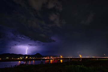 河川と街の夜景を背景にした雷雲と稲光の風景