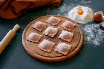 Freshly Made Ravioli Arranged on a Wooden Board Surrounded by Ingredients for Authentic Italian...
