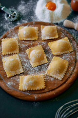 Homemade Ravioli Preparation with Flour, Egg and Kitchen Tools on Rustic Wooden Board Surrounded by Ingredients