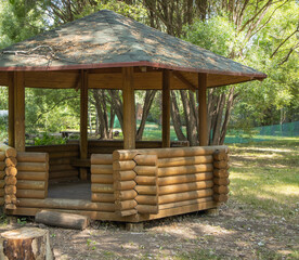An open gazebo made of round logs in the center of the park, with branches and foliage on the roof.