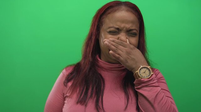 Woman covers mouth with hand and glances at wooden analog watch in studio; odor revulsion nausea disgust.