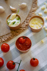 An Assortment of Fresh Ingredients Including Cherry Tomatoes, Sauces, and Garlic Set Against a Textured Tablecloth for a Culinary Delight