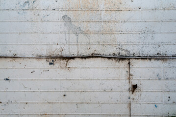 A weathered metal surface shows signs of rust and grime, with horizontal lines creating a subtle pattern across the panel. The surface appears worn, with various marks and spots adding character to it