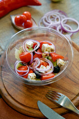 Fresh and Healthy Salad with Tomatoes, Onions, Cucumbers, and Feta Cheese Served in a Clear Bowl on a Wooden Cutting Board
