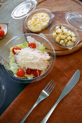 Colorful Salad with Cherry Tomatoes, Cheese, and Chicken Served on a Wooden Board Alongside Crackers and Pasta in Clear Containers
