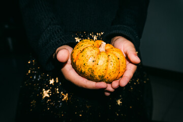 Toddler hands holding small pumpkin in witch costume during Halloween festival. Hard flash lighting