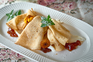 Deliciously prepared crepes served on an elegant plate, adorned with fresh mint leaves and edible flowers, accompanied by a sweet fruit jam for a delightful dessert experience.