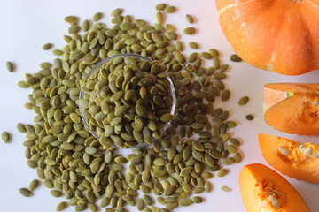 Glass jar filled with green pumpkin seeds or pepitas on a white surface, surrounded by scattered...