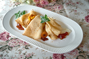 Delicious Crepes Served with Sweet Jam and Garnished with Fresh Mint and Flower Petals on a Floral Tablecloth Setting