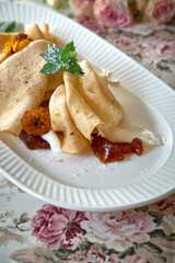 Delicate Crepes Filled with Sweet Jam and Cream, Garnished with Mint Leaves on an Elegant Floral Table Setting