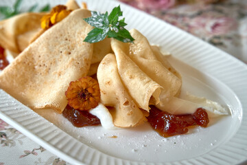 Delicately Plated Crepes Decorated with Fresh Mint, Edible Flowers, and a Sweet Fruit Preserve Glaze for a Delicious Dessert Presentation
