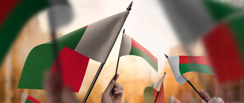 Madagascar flags in their hands on a blurred urban background