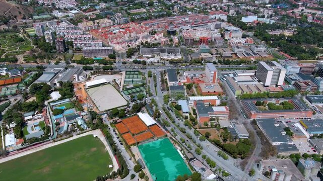 Drone view over Les Corts showing clay tennis courts, field hockey turf, polo and equestrian arenas beside university buildings and roads in sunny Barcelona, Spain.