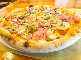 Delicious italian pizza with ham, artichokes, and mushrooms on wooden table