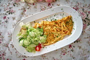 Deliciously Prepared Omelette Plated with Fresh Salad Garnished with Herbs on a Floral-Patterned Tablecloth Ideal for Breakfast or Brunch Lovers