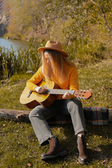 Portrait of smiling caucasian artist plays wooden acoustic guitar in autumnal park. Young...