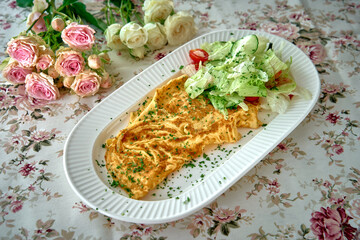 A Delicious Plate of Creamy Omelette Accompanied by Fresh Salad and Decorated with Beautiful Blooms in the Background